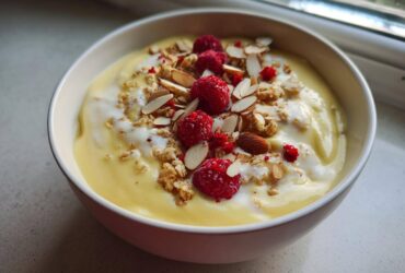 Close-up of a Creamy Vanilla Protein Smoothie Bowl topped with raspberries, granola, and sliced almonds.