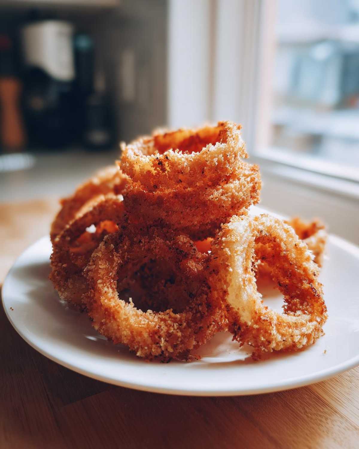 A stack of golden brown, crispy Air Fryer Onion Rings piled on a small white plate.