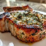Close-up of a juicy, crispy air fryer pork chop topped generously with glistening garlic butter and herbs.