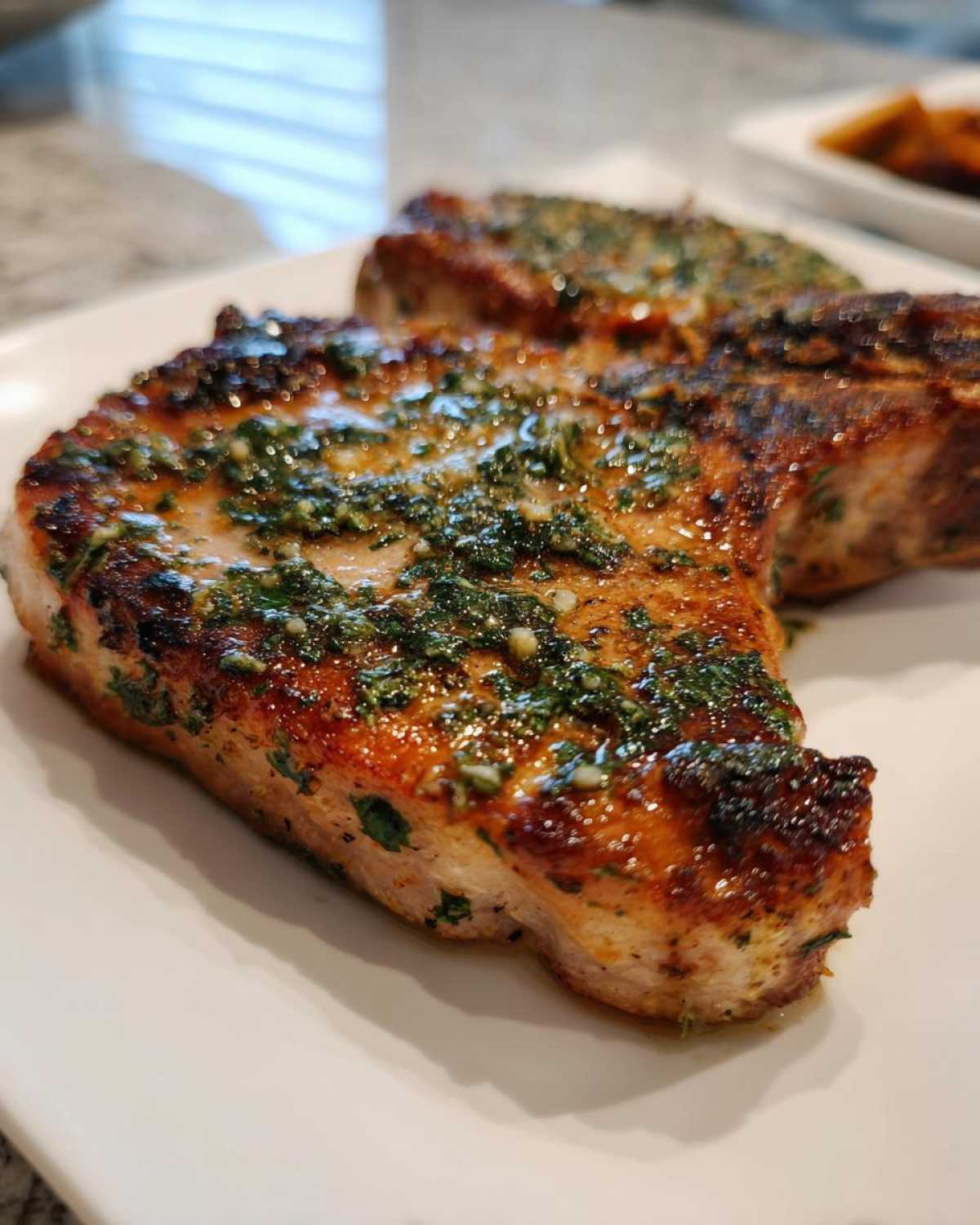 Close-up of a juicy, browned Crispy Air Fryer Pork Chop topped with glistening garlic butter and herbs.