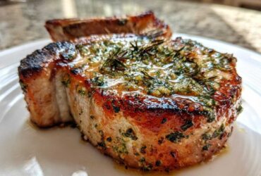 Close-up of a juicy, crispy air fryer pork chop topped generously with glistening garlic butter and herbs.