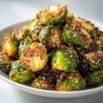 Close-up of perfectly roasted Crispy Parmesan Brussels Sprouts piled high in a white serving dish.