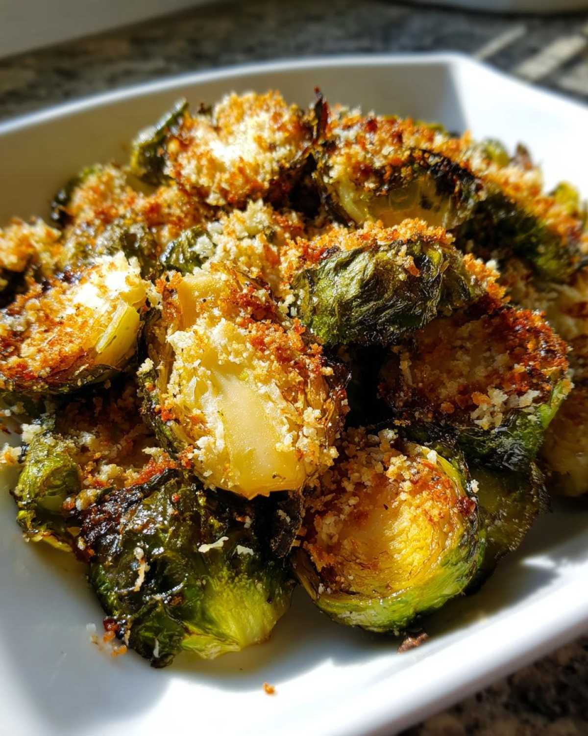 A close-up of perfectly roasted Crispy Parmesan Brussels Sprouts piled high in a white serving dish.