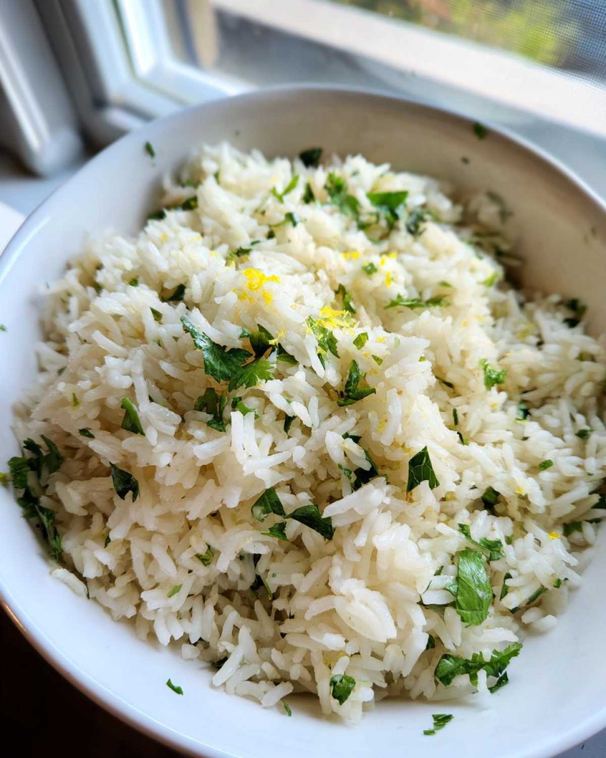Close-up of fluffy Cilantro Lime Rice mixed with chopped cilantro and bright yellow lime zest in a white bowl.