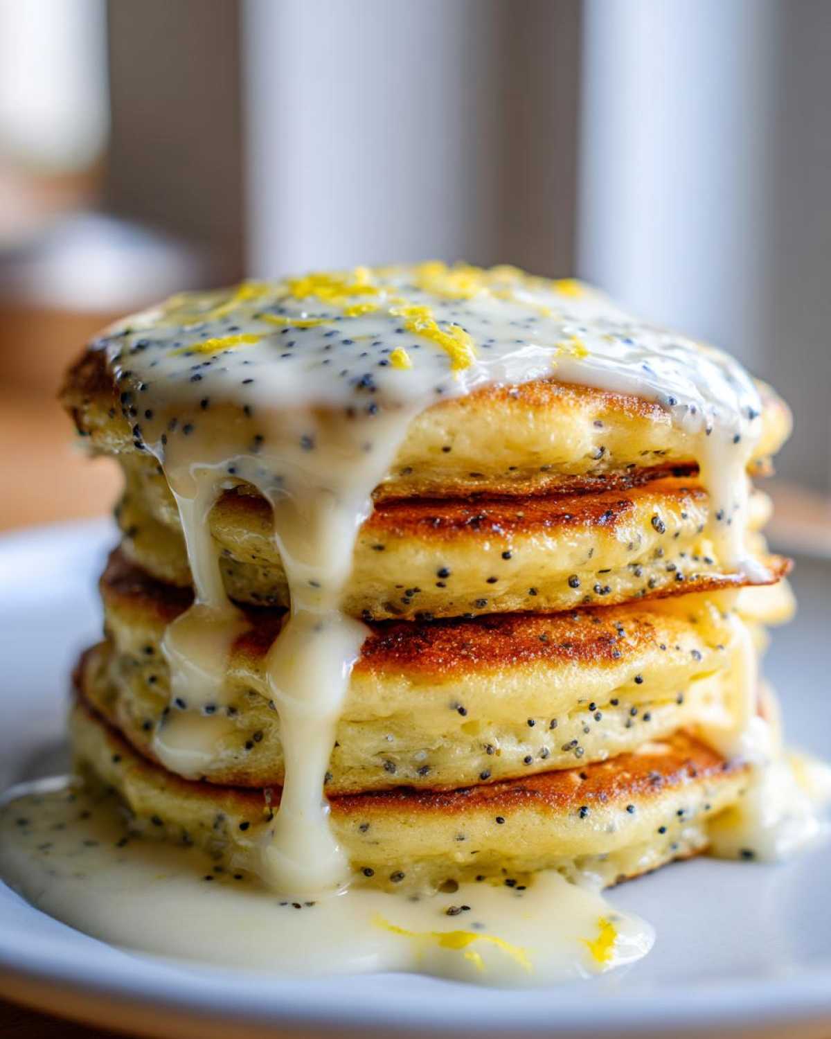 Close-up of a stack of fluffy Vegan Lemon Poppy Seed Pancakes dripping with white lemon glaze and topped with zest.