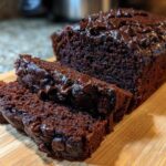 A close-up of fudgy Vegan Chocolate Banana Bread, sliced and topped with melted chocolate chips on a wooden board.