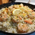 Close-up of Garlic Butter Shrimp and Rice Skillet topped with lemon slices and parsley in a black cast iron pan.