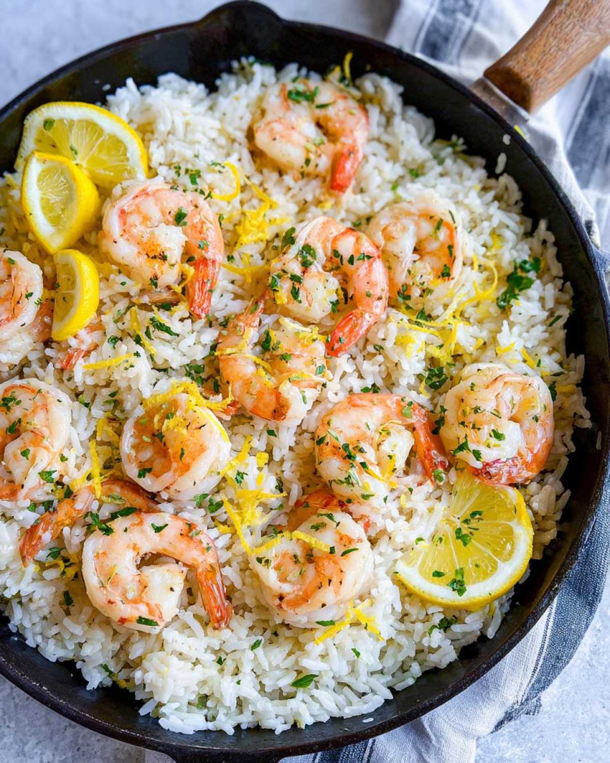 Close-up of Garlic Butter Shrimp and Rice Skillet topped with cooked shrimp, lemon zest, and parsley.