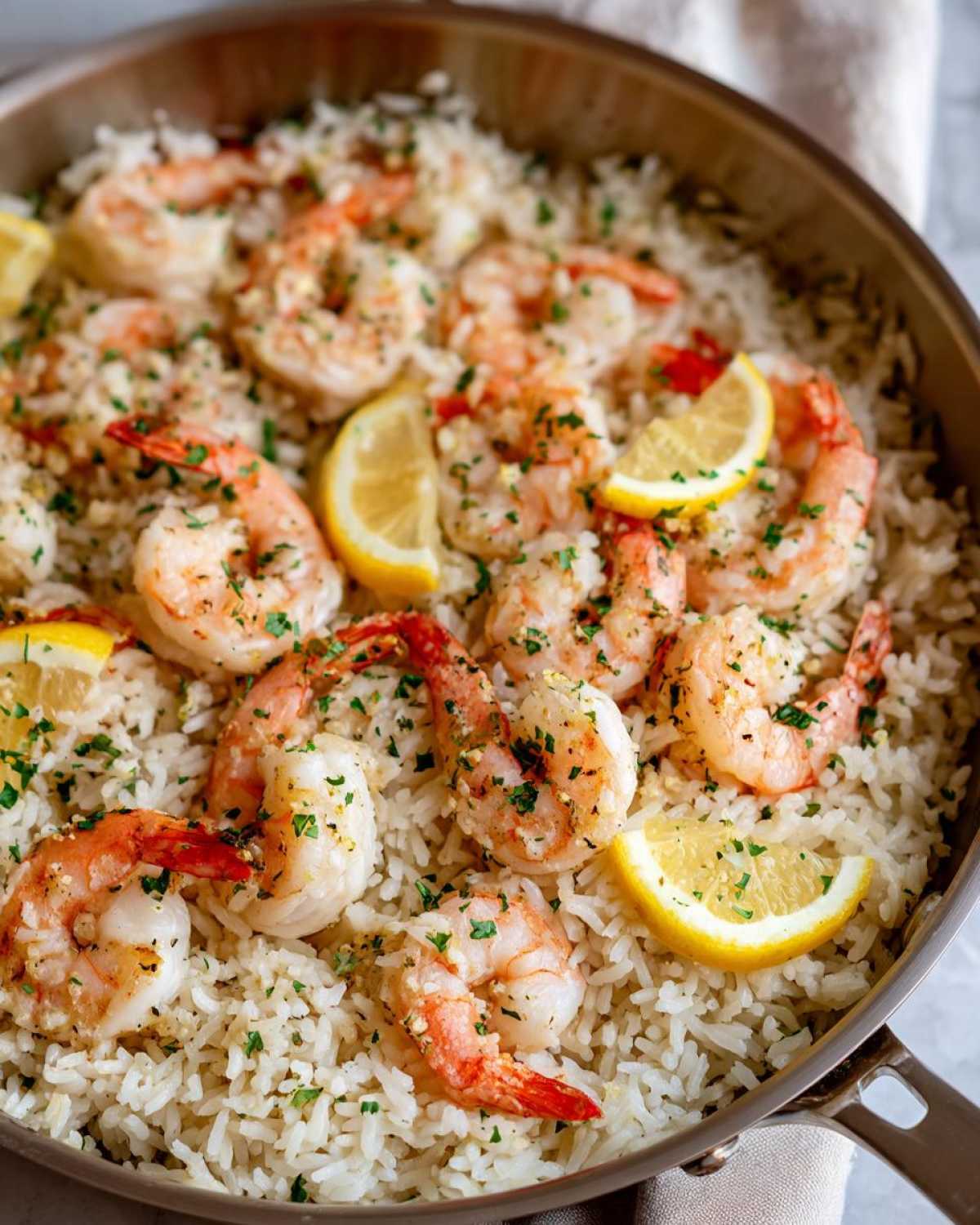 Close-up of Garlic Butter Shrimp and Rice Skillet topped with lemon wedges and parsley.