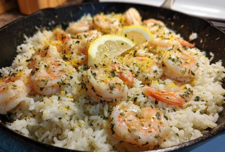 Close-up of Garlic Butter Shrimp and Rice Skillet topped with lemon slices and parsley in a black cast iron pan.