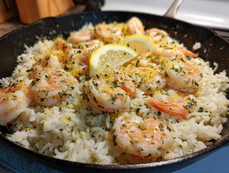 Close-up of Garlic Butter Shrimp and Rice Skillet topped with lemon slices and parsley in a black cast iron pan.