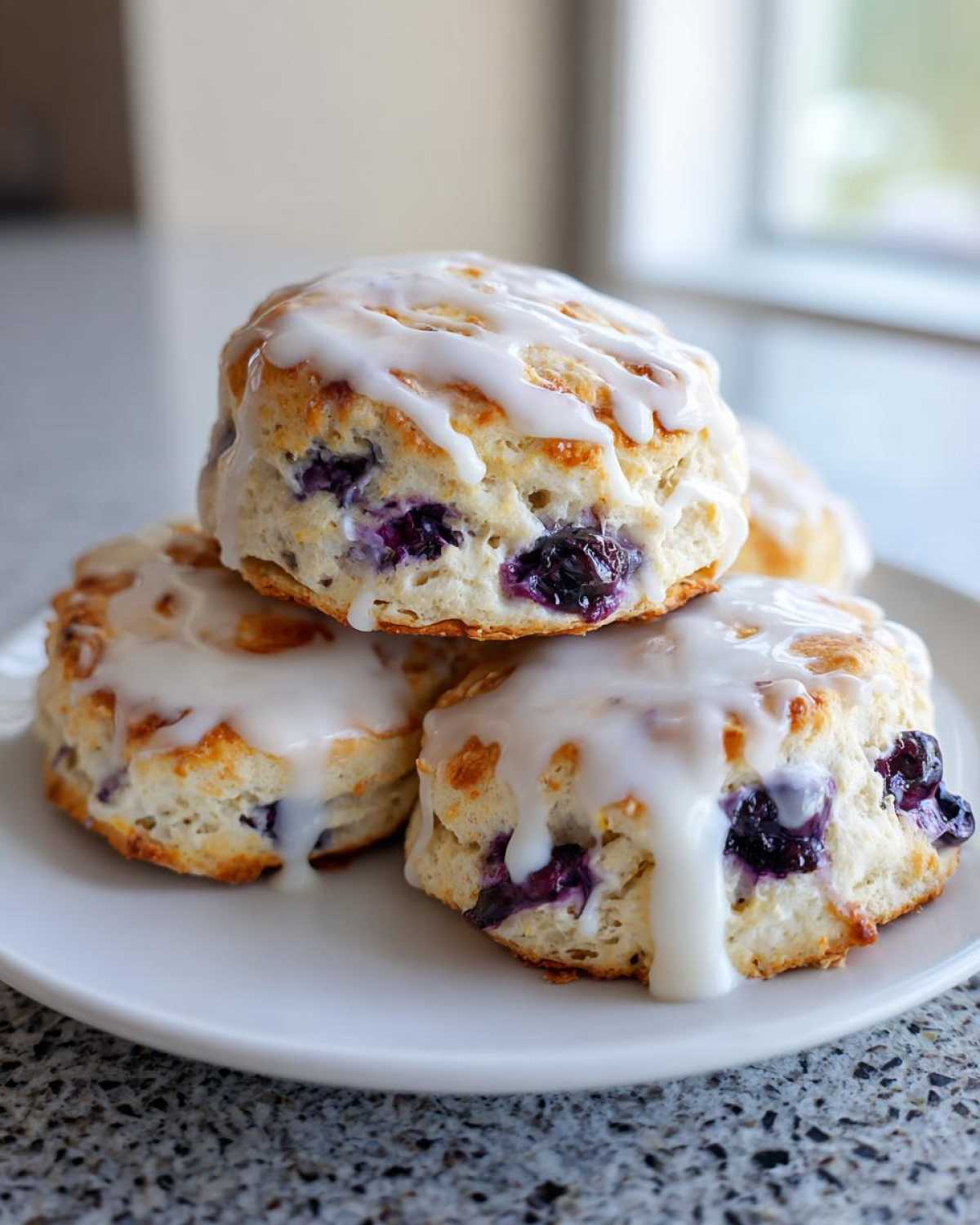 A stack of three freshly baked Blueberry Lemon Scones topped with thick white lemon glaze.