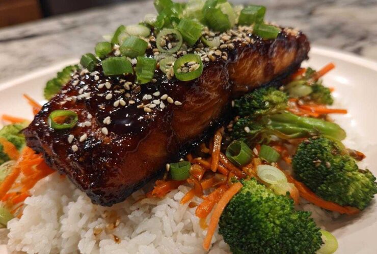 Close-up of a glazed Teriyaki Salmon fillet served over white rice with broccoli, shredded carrots, and green onions.