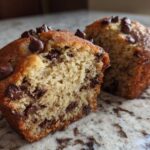 A Gluten-Free Banana Chocolate Chip Muffin cut in half showing the moist interior filled with chocolate chips.