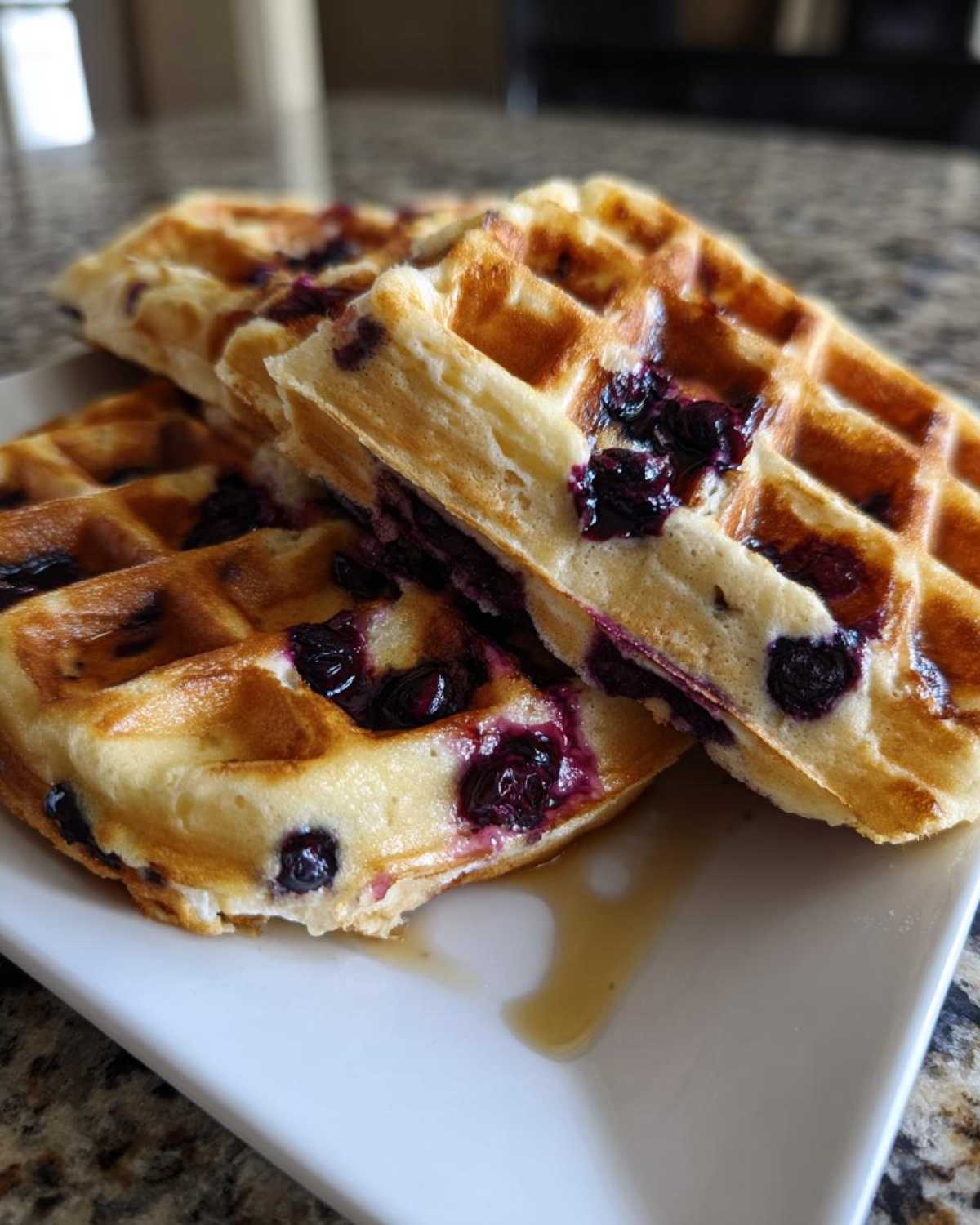 Close-up of stacked, golden Gluten-Free Blueberry Waffles drizzled with syrup on a white plate.