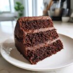 Close-up of a rich, moist slice of three-layer Gluten-Free Chocolate Cake with dark frosting.
