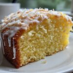 Close-up of a moist slice of Gluten-Free Lemon Coconut Cake topped with white glaze and toasted coconut flakes.