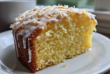 Close-up of a moist slice of Gluten-Free Lemon Coconut Cake topped with white glaze and toasted coconut flakes.