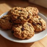 A close-up of several freshly baked Gluten-Free Oatmeal Raisin Cookies piled on a white plate.