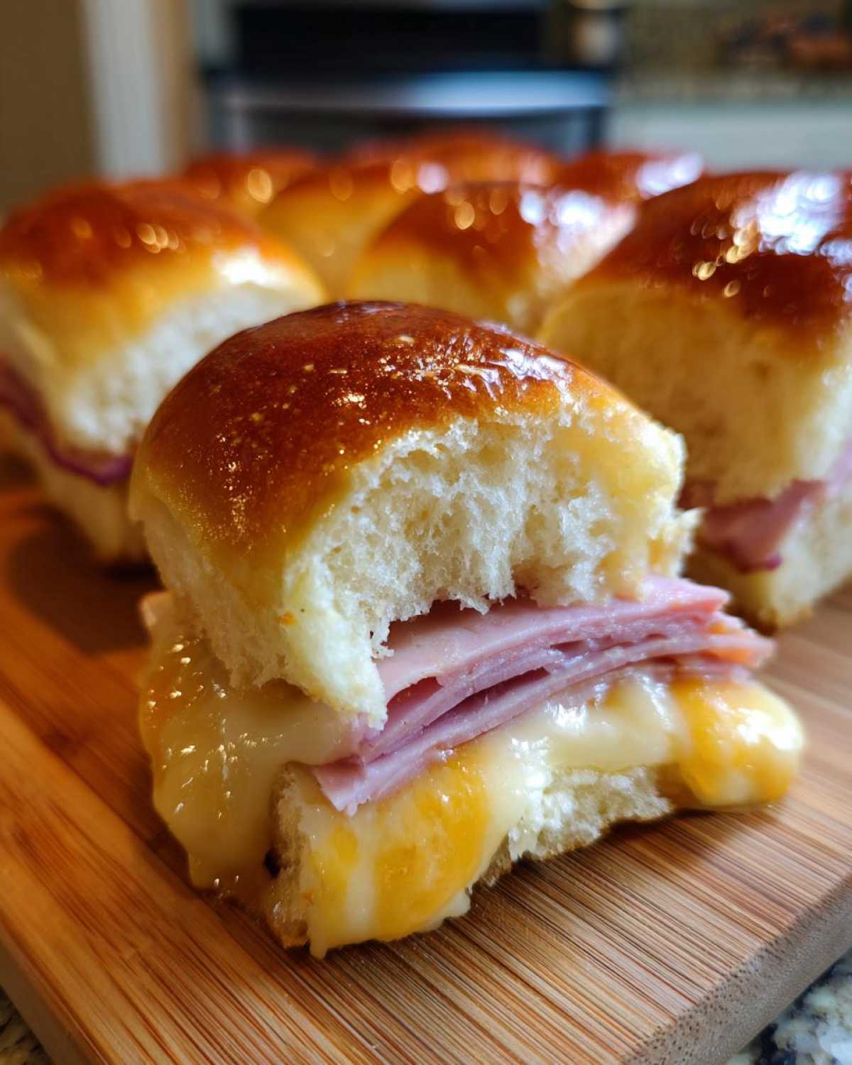 Close-up of a Hawaiian Roll Ham and Cheese Slider with melted cheese oozing out, showing layers of ham.