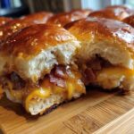 Close-up of a Hawaiian Roll Ham and Cheese Slider cut in half, showing melted cheese and bacon filling.