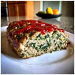 A thick slice of Healthy Turkey Spinach Meatloaf, showing the green spinach mixed into the turkey, topped with bright red ketchup.