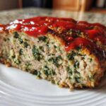 A thick slice of Healthy Turkey Spinach Meatloaf topped with a bright red ketchup glaze, showing green spinach throughout the turkey mixture.