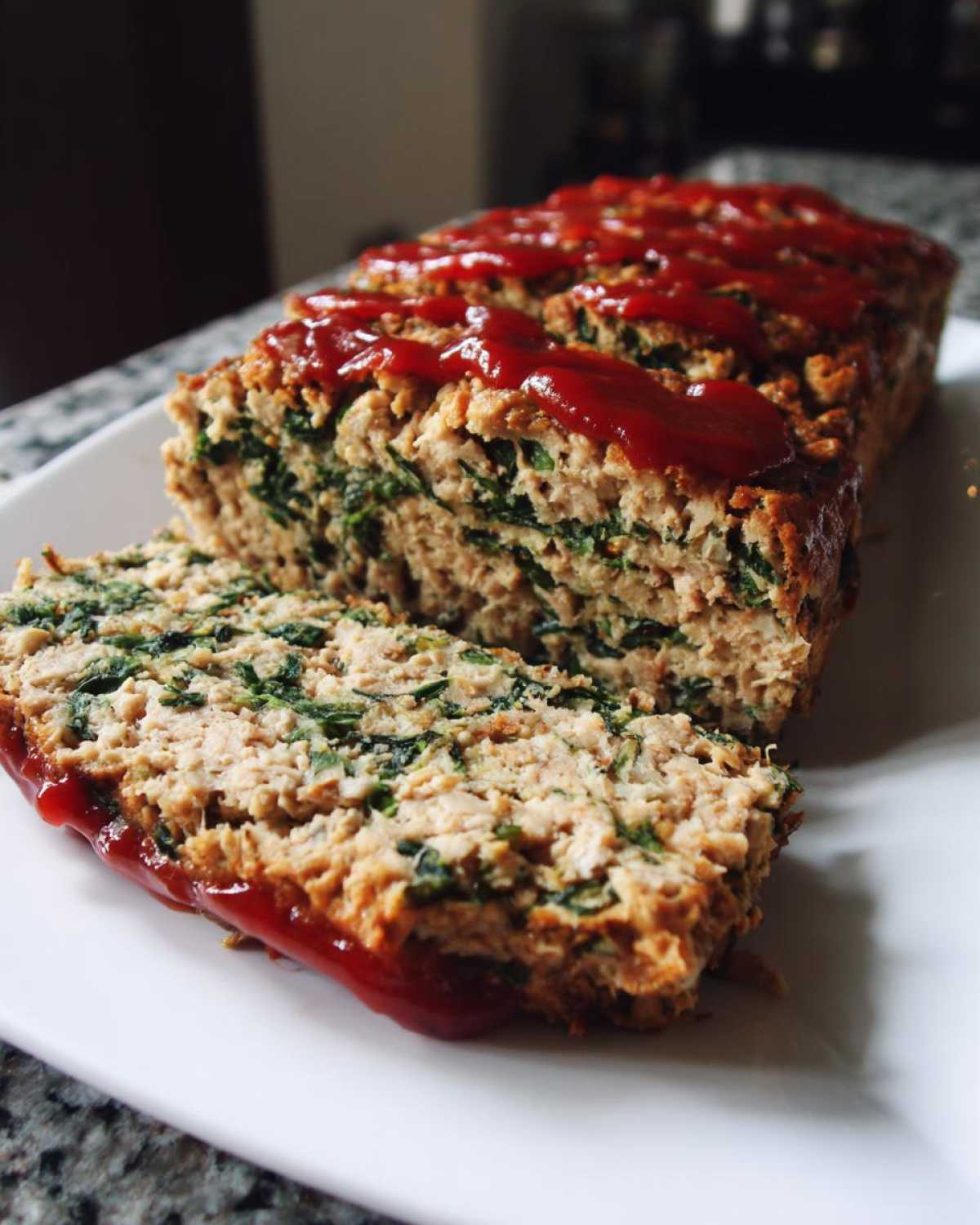 A sliced loaf of Healthy Turkey Spinach Meatloaf topped with a drizzle of ketchup glaze on a white plate.
