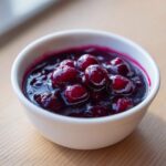 A small white bowl filled with thick, rich Homemade Blueberry Syrup featuring whole, glossy blueberries.