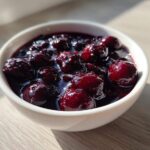 Close-up of thick, rich Homemade Blueberry Syrup with whole berries in a small white bowl.