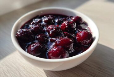 Close-up of thick, rich Homemade Blueberry Syrup with whole berries in a small white bowl.