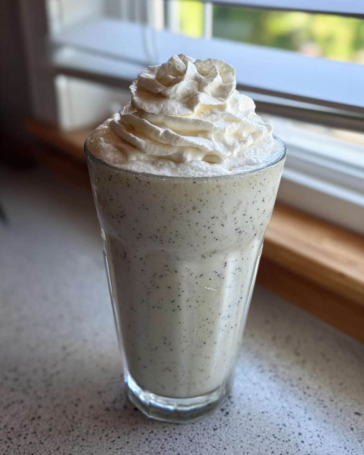 A tall glass of Homemade Vanilla Bean Frappuccino topped with a swirl of whipped cream.