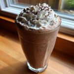 A tall glass of rich, blended Homemade Vanilla Bean Frappuccino topped with whipped cream and chocolate shavings.