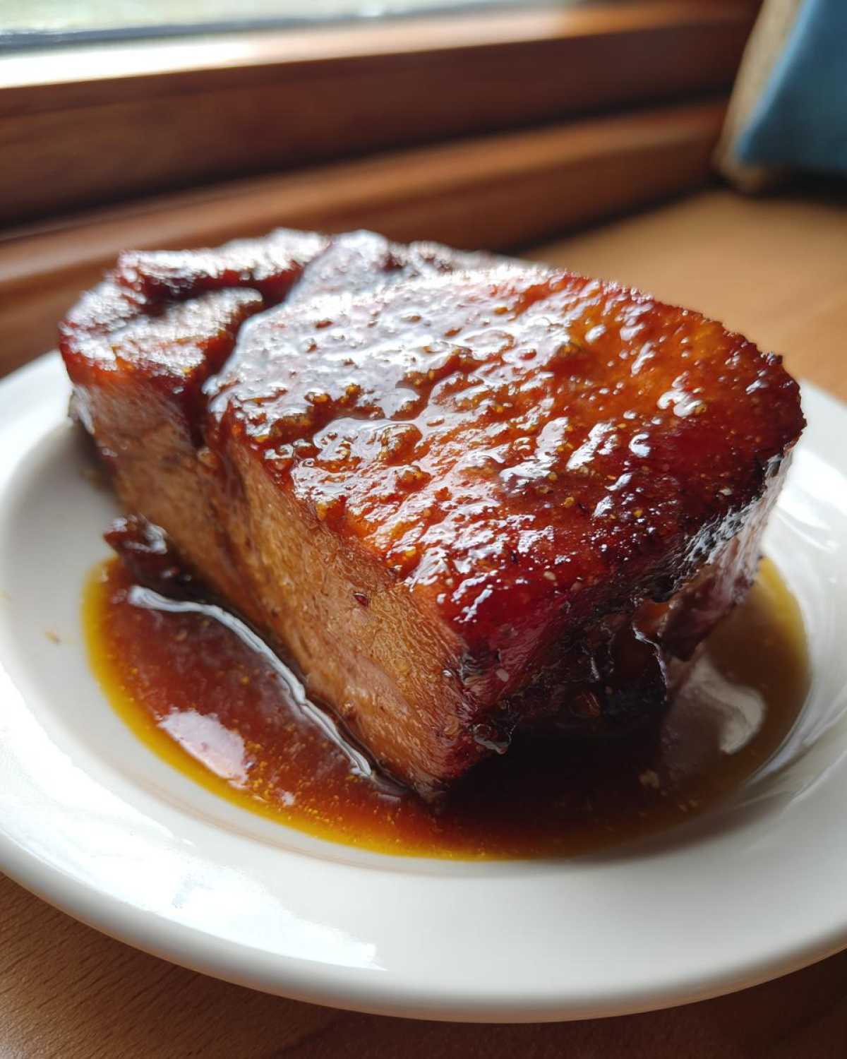 Close-up of a thick, square Honey Glazed Ham Steak glistening with thick, dark glaze on a white plate.