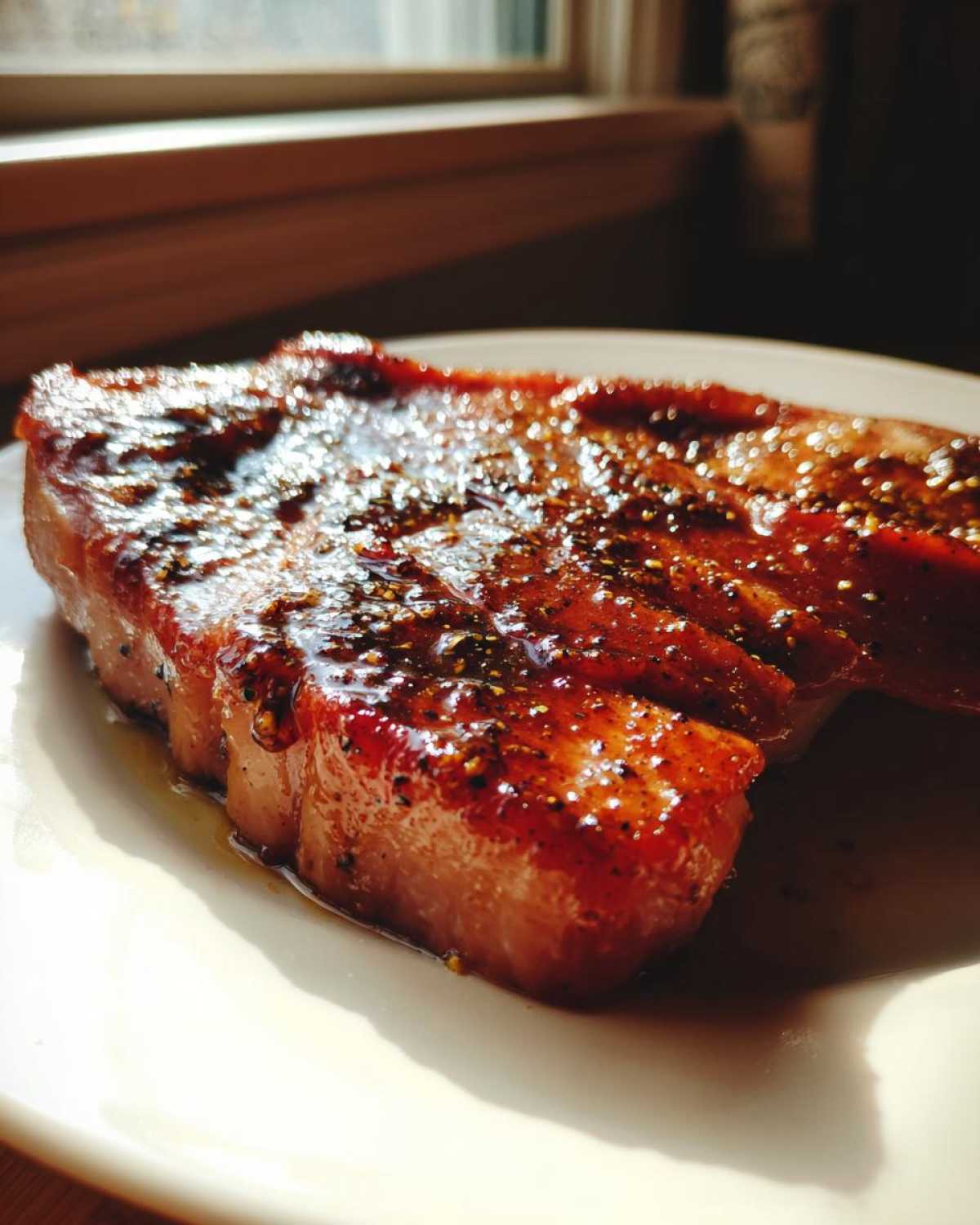 A close-up of a thick Honey Glazed Ham Steak in the Skillet, glistening with a dark, sweet glaze and cracked black pepper.