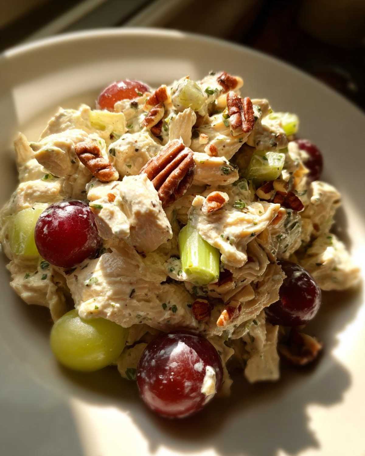A close-up, brightly lit serving of Honey Mustard Chicken Salad with Grapes, pecans, and celery chunks on a white plate.