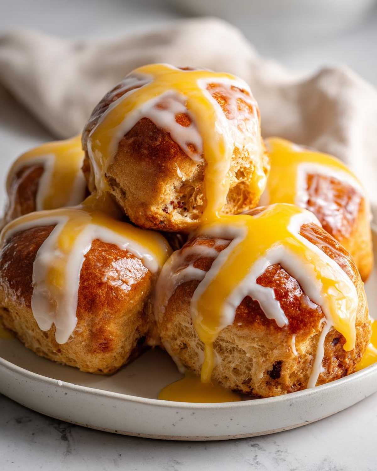 A stack of freshly baked Hot Cross Buns with Orange Glaze drizzled over the white icing crosses.