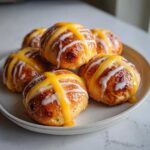 A stack of freshly baked Hot Cross Buns with Orange Glaze, drizzled with white icing.
