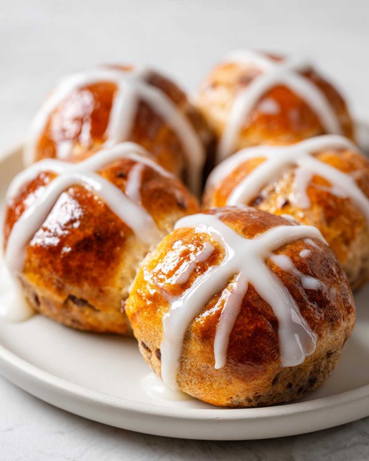 A close-up of several freshly baked Hot Cross Buns with a thick, white orange glaze cross on top.