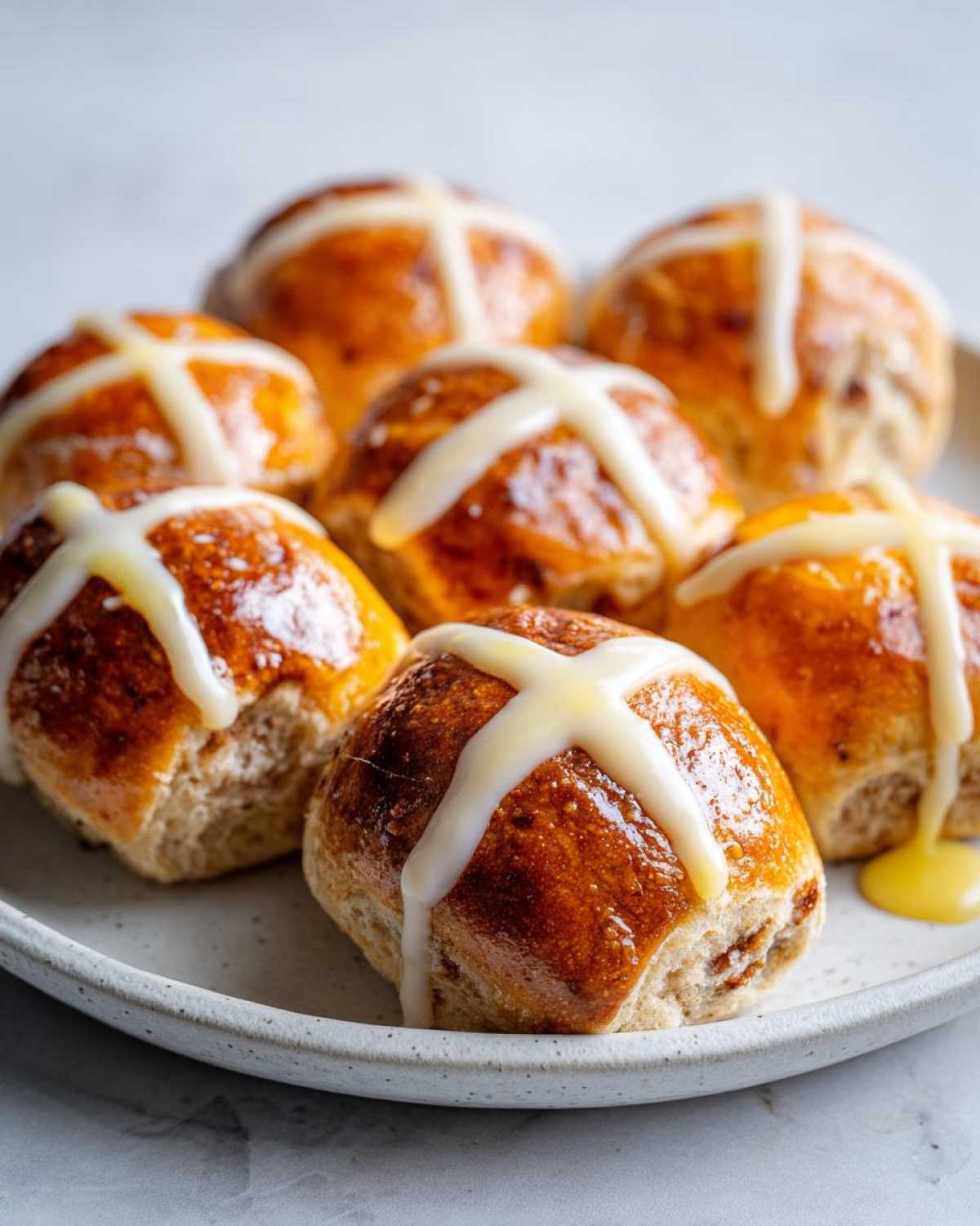 A close-up of several freshly baked Hot Cross Buns with Orange Glaze drizzled over the white crosses.