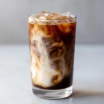 Close-up of an Iced Honey Almond Milk Latte with milk swirling dramatically into dark coffee over ice.