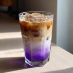 A tall glass of Iced Lavender Latte showing distinct purple, white, and brown layers over ice.