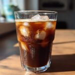 Close-up of a tall glass filled with a dark Iced Mocha and large ice cubes, glistening in sunlight.
