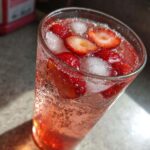 Close-up of a tall glass filled with Iced Strawberry Lemon Tea, sliced strawberries, and ice cubes.