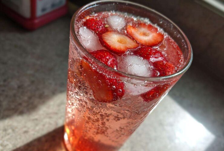 Close-up of a tall glass filled with Iced Strawberry Lemon Tea, sliced strawberries, and ice cubes.