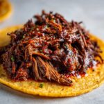 Close-up of juicy, shredded Instant Pot Beef Barbacoa piled high on a warm corn tortilla.
