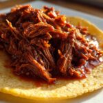 Close-up of shredded, saucy Instant Pot Beef Barbacoa piled high on a warm corn tortilla.