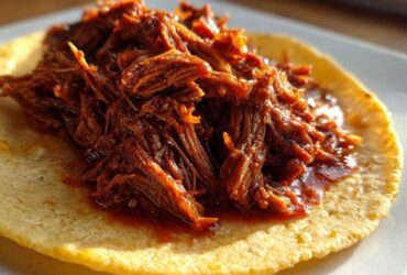 Close-up of shredded, saucy Instant Pot Beef Barbacoa piled high on a warm corn tortilla.