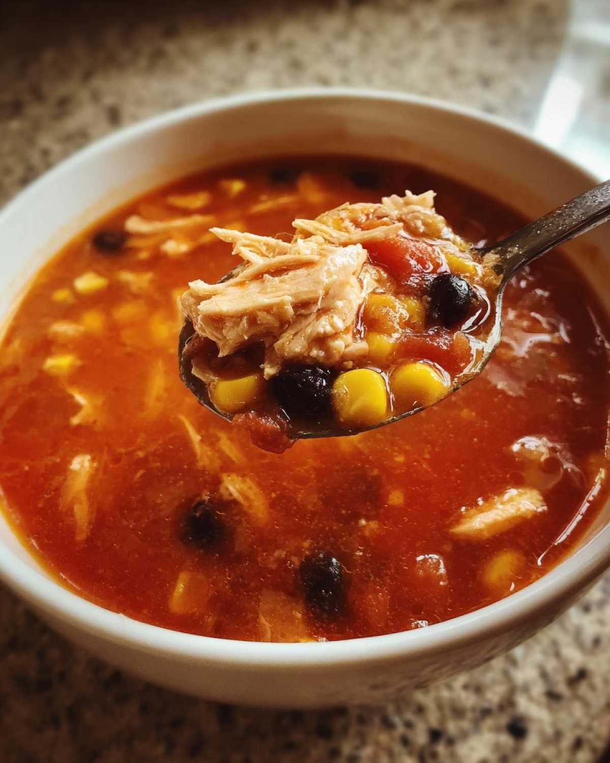 A spoonful lifted from a bowl of Instant Pot Chicken Tortilla Soup, showing shredded chicken, corn, and black beans.