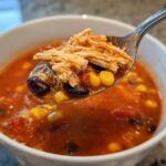 A spoonful of Instant Pot Chicken Tortilla Soup showing shredded chicken, black beans, and corn being lifted from a white bowl.